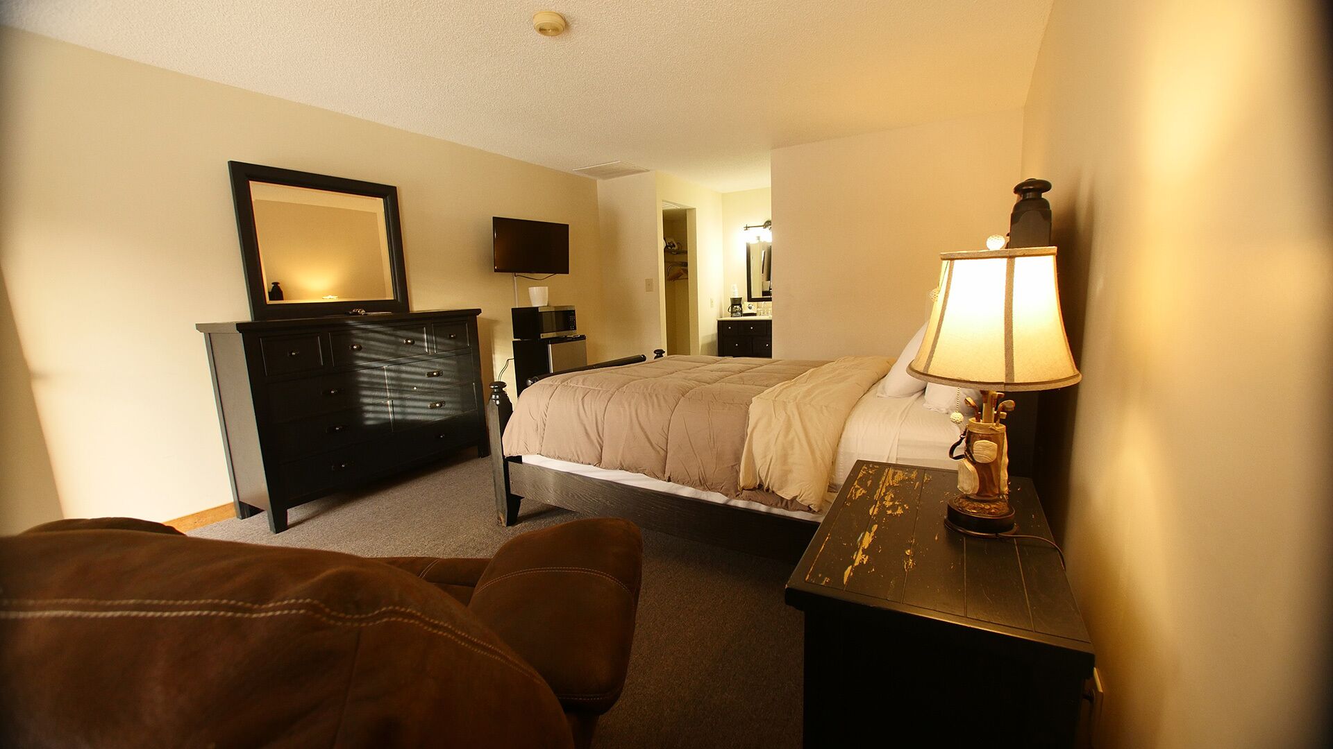 Une chambre d’hôtel avec un lit, une commode, une table de chevet avec une lampe et un miroir au mur.