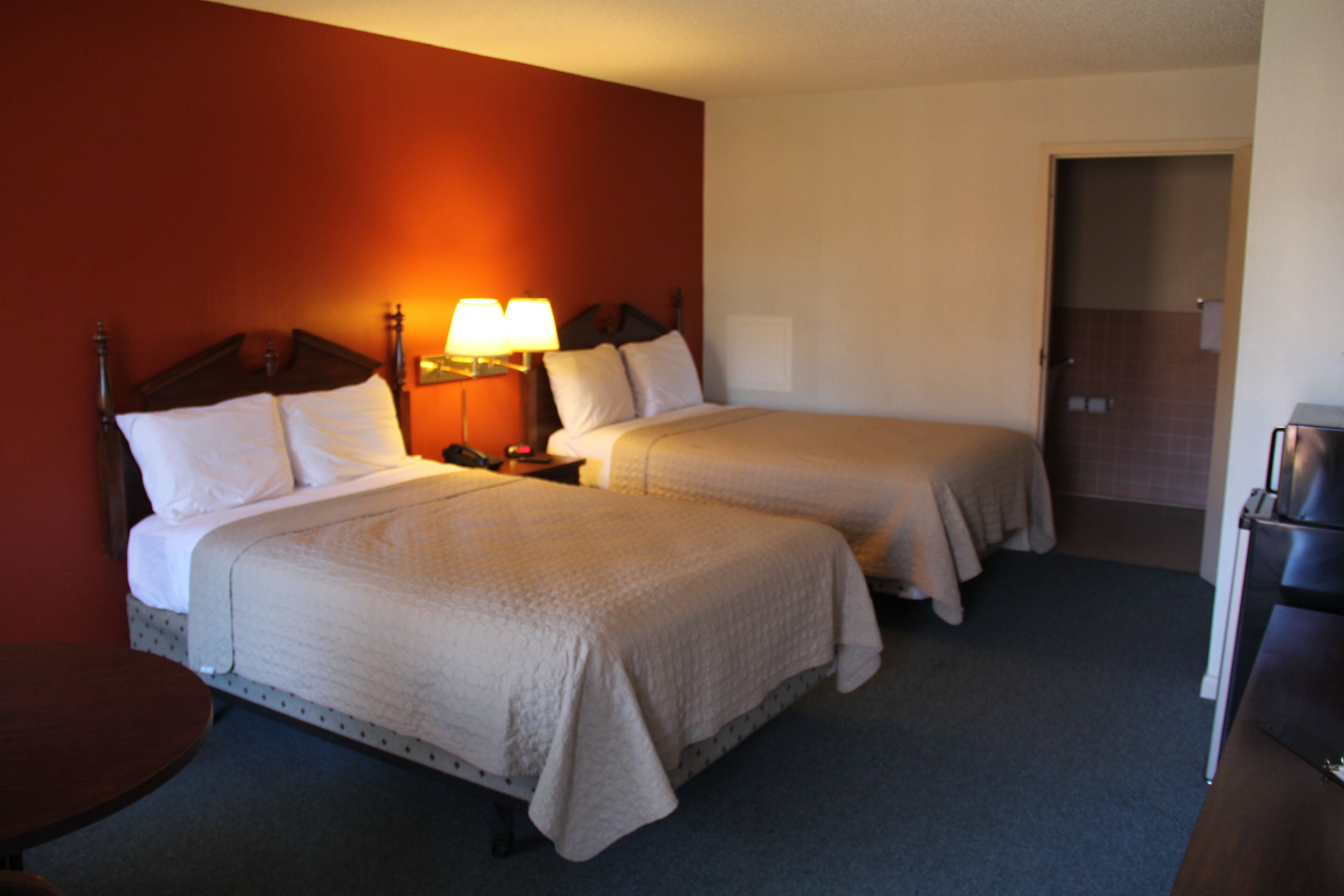 A hotel room with two beds, a nightstand with lamps, a small table, and a refrigerator.