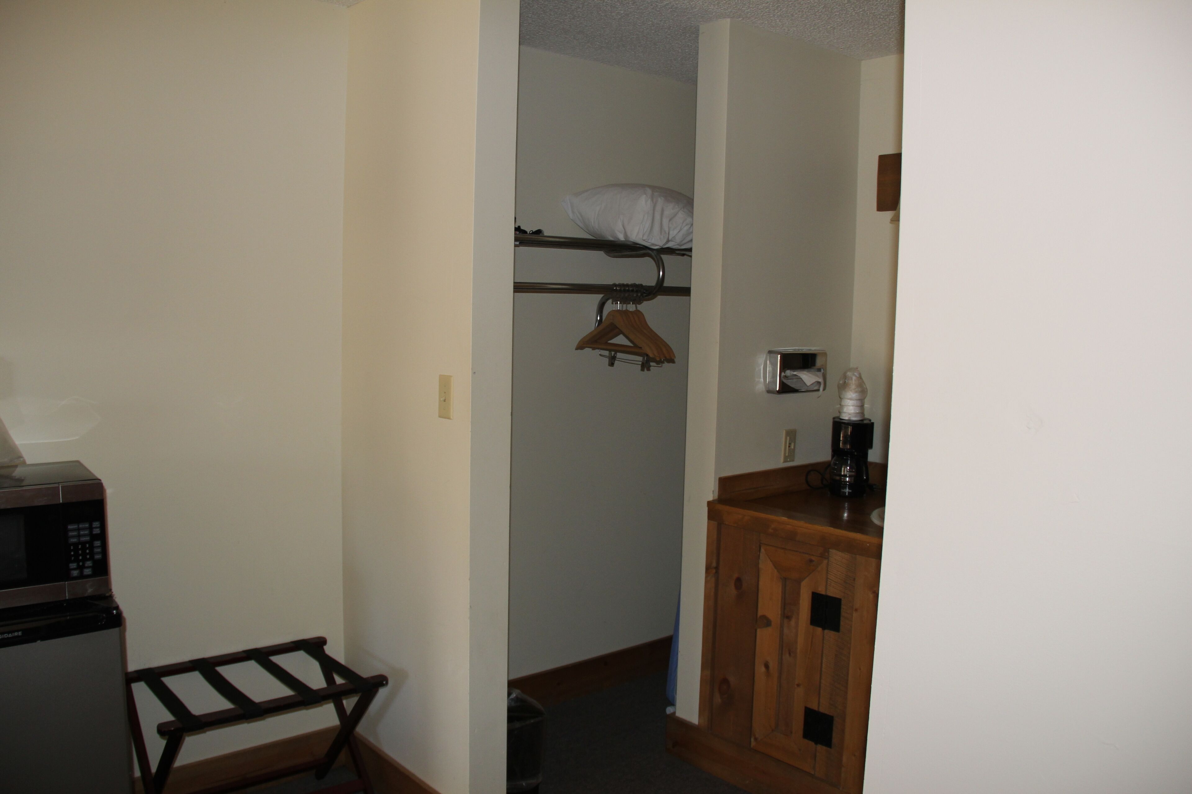 A compact kitchen with a microwave, a wooden drying rack, and a wooden cabinet.
