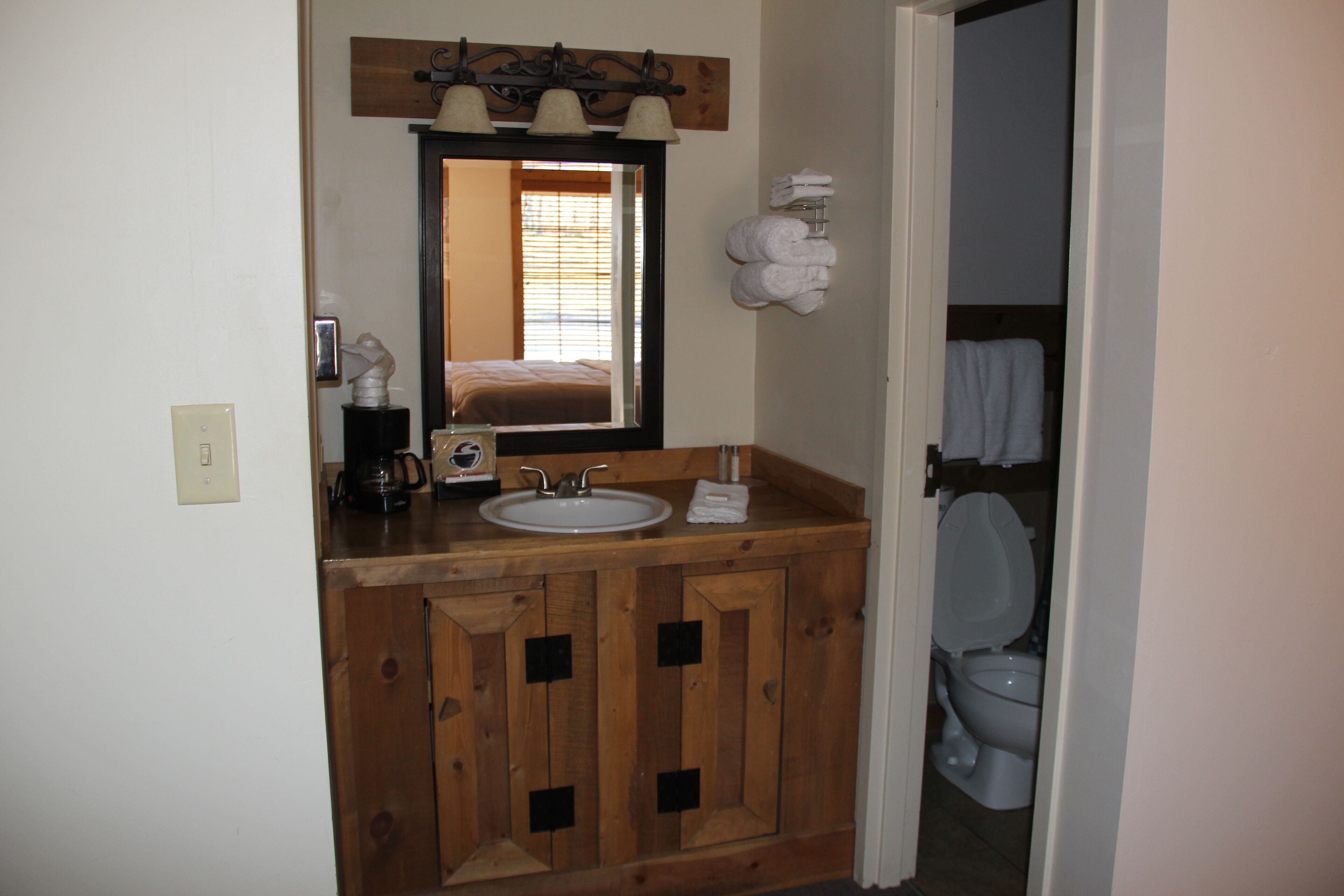 A bathroom with a wooden vanity, a sink, a mirror, and a toilet.