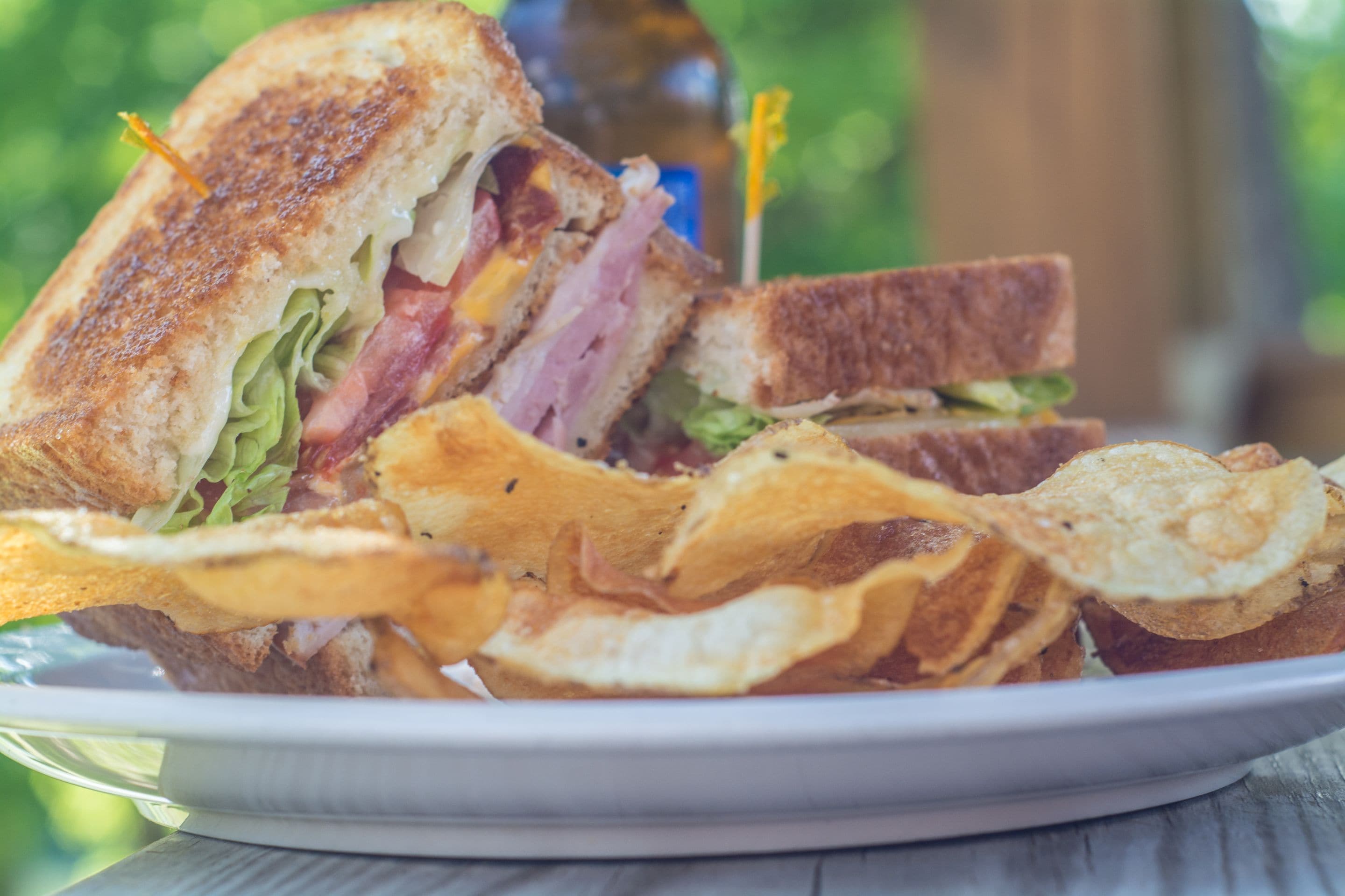 A sandwich with visible layers of meat, cheese, and lettuce, accompanied by potato chips on a plate.