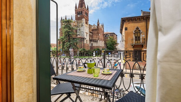 A balcony with a table set for two, overlooking a historic church with a tall bell tower. - Dimore Verona (Verona)