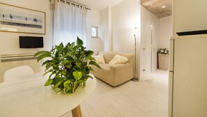 A modern living room with a white sofa, a dining table with a plant, a flat-screen TV, and a large window with curtains. - Dimore Verona (Verona)