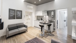 A modern kitchen with a built-in oven, a dining area with a bar stool, and a grey sofa. - Dimore Verona (Verona)