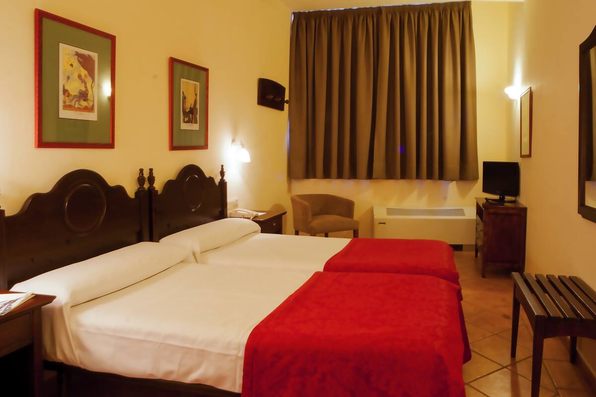 A hotel room with two beds, a desk, a chair, a TV, and a window with curtains.