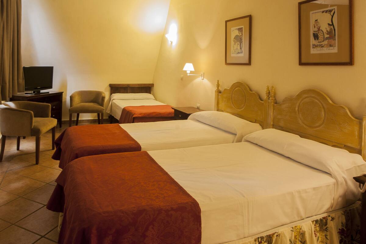 A hotel room with two single beds, a desk with a television, a chair, and a lamp.
