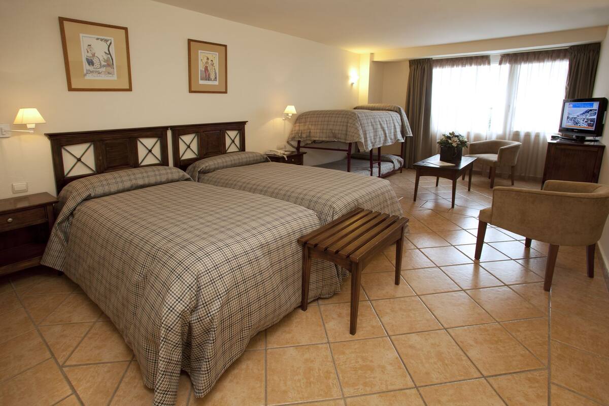 A hotel room with two beds, a desk, a chair, and a television.