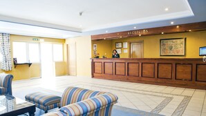 Un área de recepción con un mostrador de madera, una recepcionista, sofás a rayas y un cuadro grande en la pared.