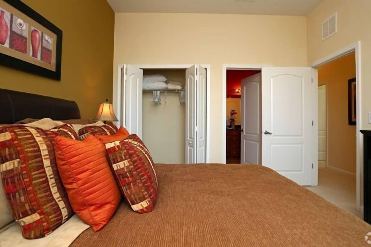 Ein Schlafzimmer mit einem Bett, Kissen, einem Nachttisch, einer Lampe und einer Tür zu einem Badezimmer.