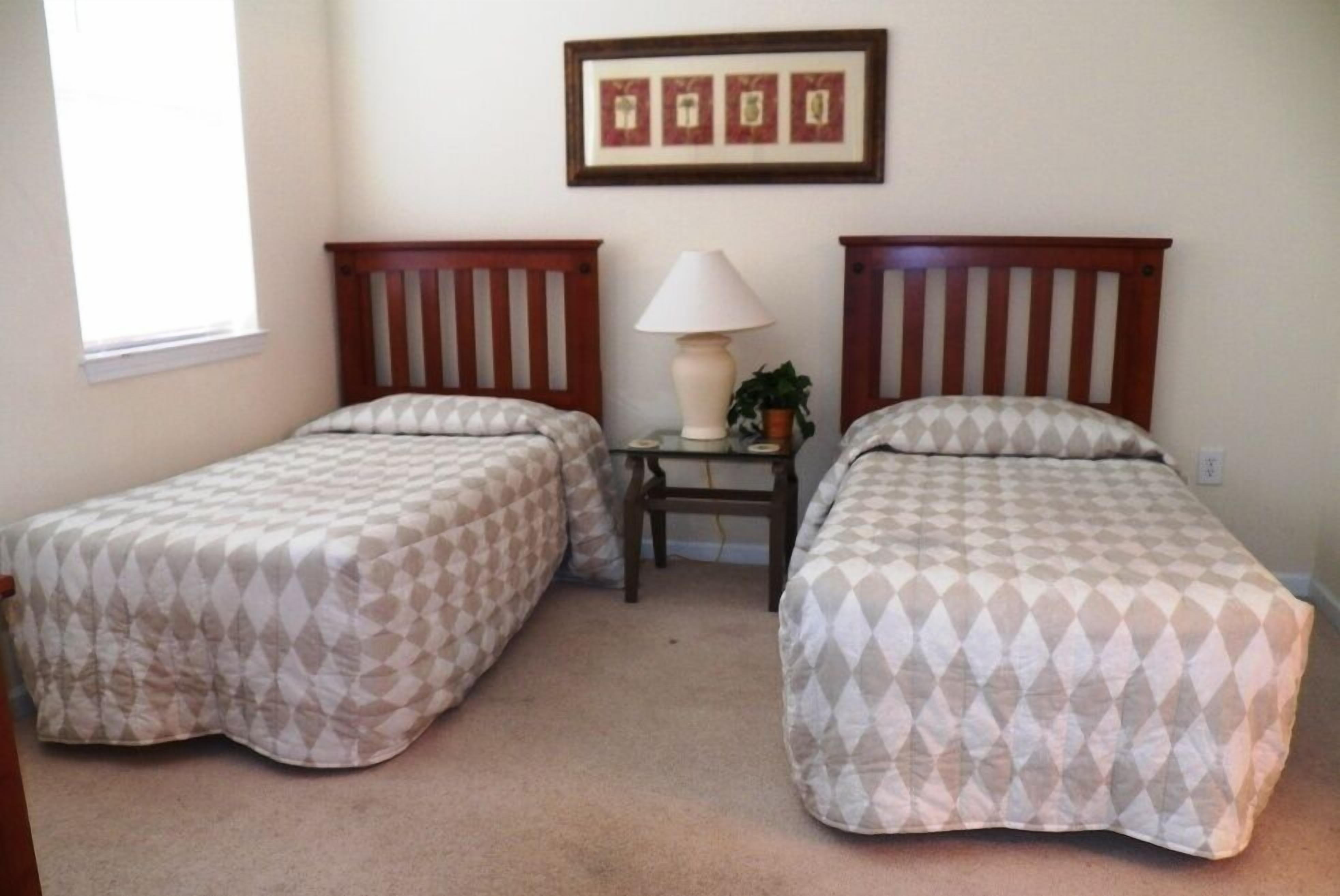 A bedroom with two single beds, a nightstand with a lamp, and a framed picture on the wall.