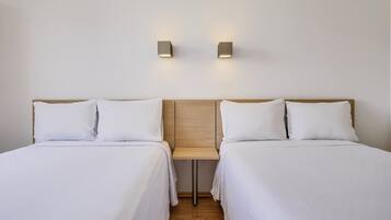 Une chambre d’hôtel avec deux lits simples, une petite table et deux lampes fixées au mur.