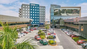 Un hotel con un llamativo letrero que dice 'one hotel', un estacionamiento con varios autos y edificios modernos al fondo.