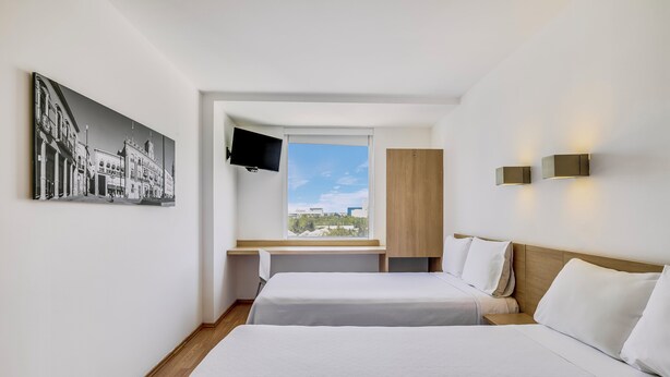 Habitación de hotel con dos camas, un ventanal con vistas, un televisor montado y una lámpara de pared.
