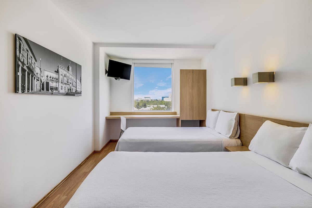 A hotel room with two beds, a large window with a view, a mounted TV, and a wall-mounted light fixture.