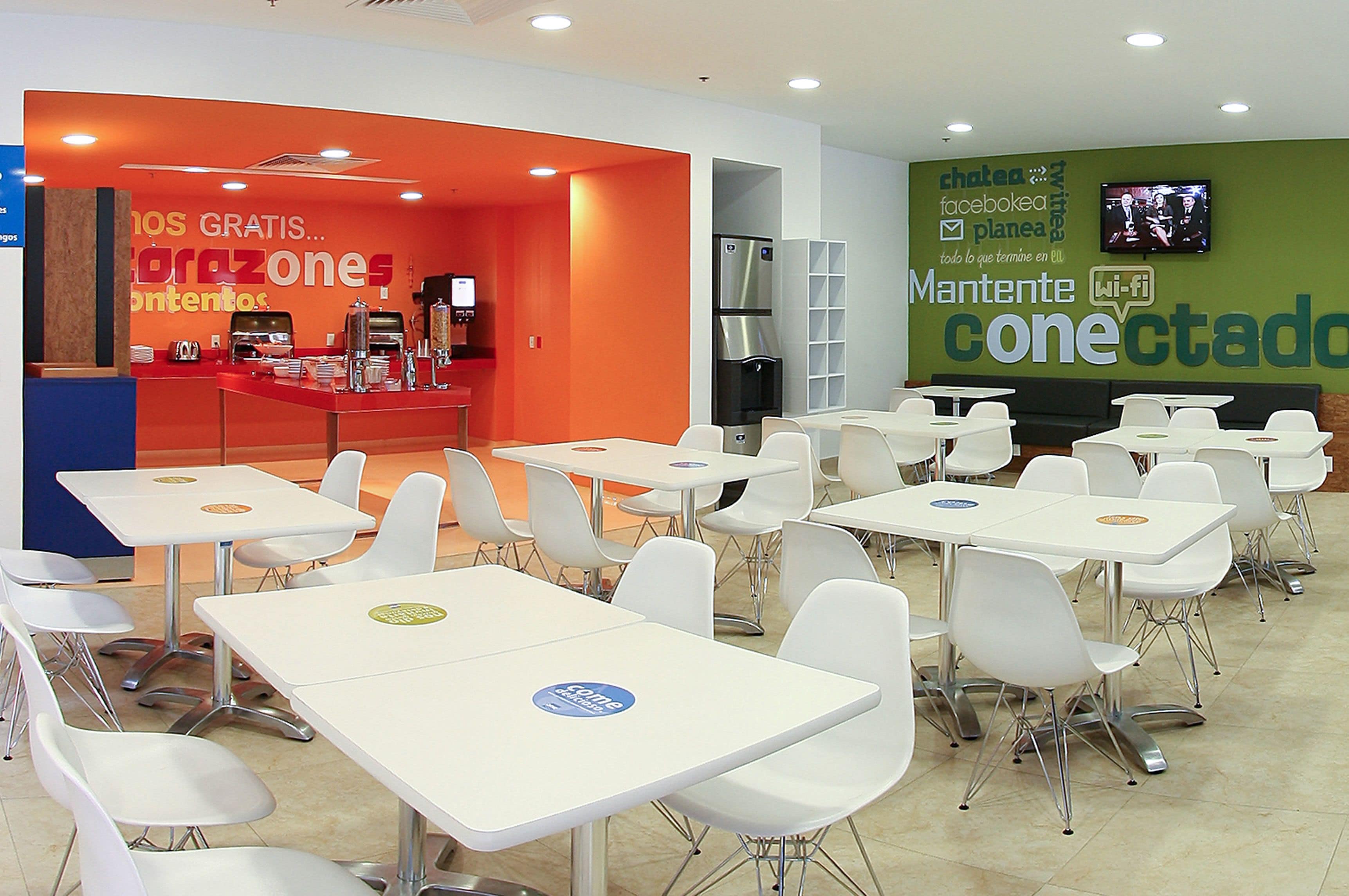 Een moderne cafetaria met witte tafels en stoelen, een rode balie met koffiehoek, en een groene muur met een Wi-Fi-bordje.