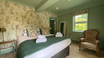 A bedroom with a large bed, a chair, a nightstand, a mirror, and a window with daylight.