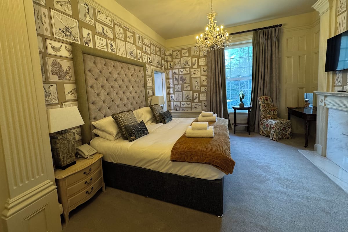 Une chambre à coucher avec un grand lit, un lustre, un bureau, une chaise et une cheminée.