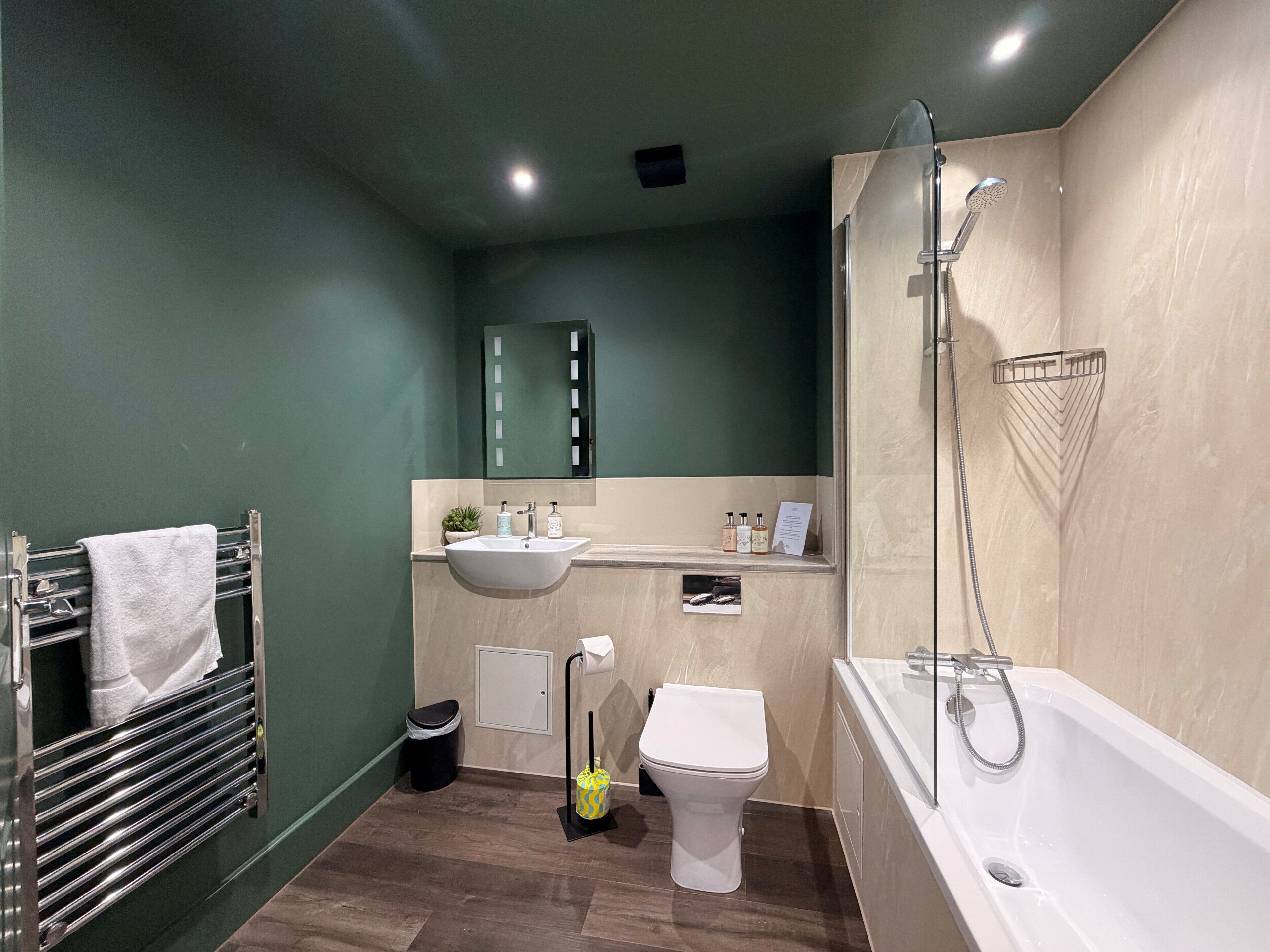 A modern bathroom with a sink, toilet, and bathtub, featuring a green wall and wooden flooring.