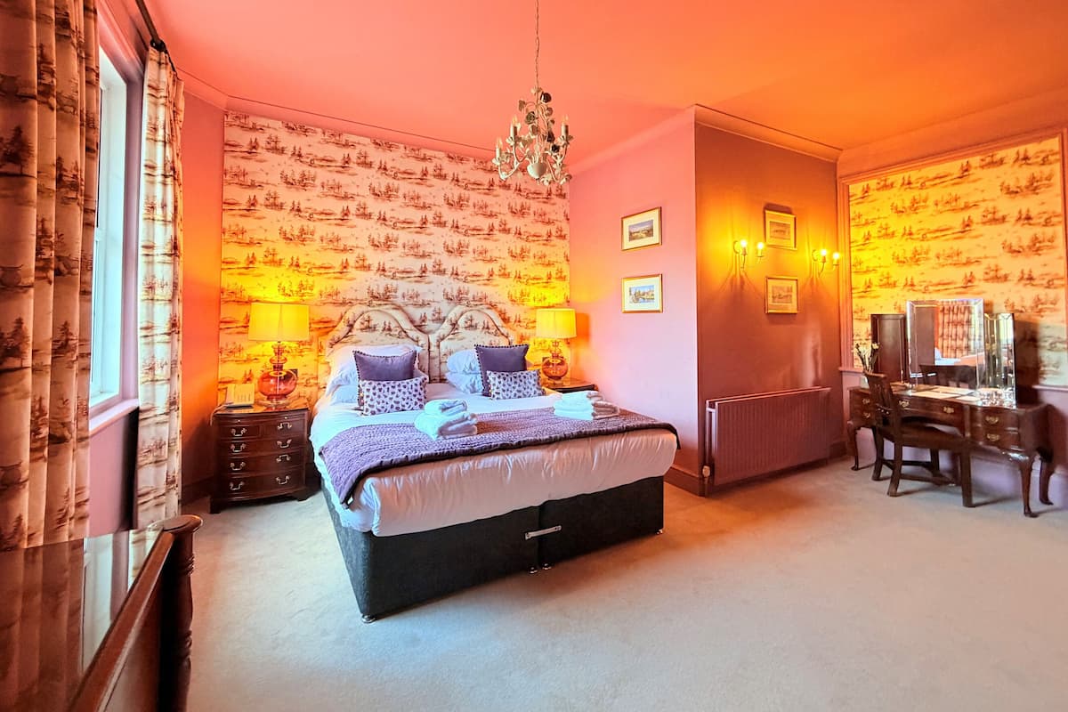 Une chambre à coucher comprenant un lit, des tables de chevet, un bureau avec une chaise, une commode et un lustre.