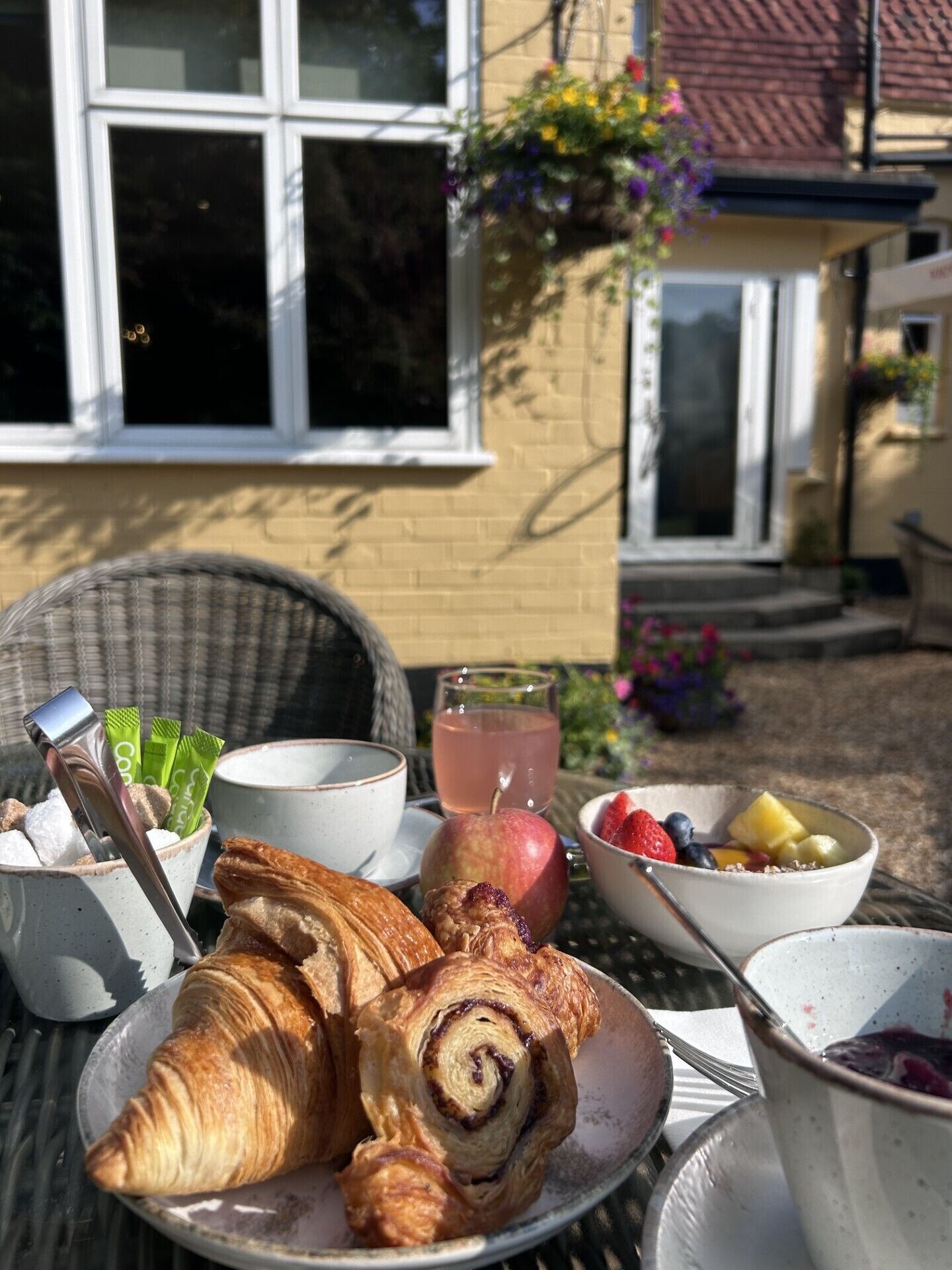 Een ontbijttafel met croissants, een schaal fruit, een glas sap en een kop koffie.