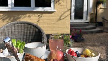 Een ontbijttafel met croissants, een schaal fruit, een glas sap en een kop koffie.