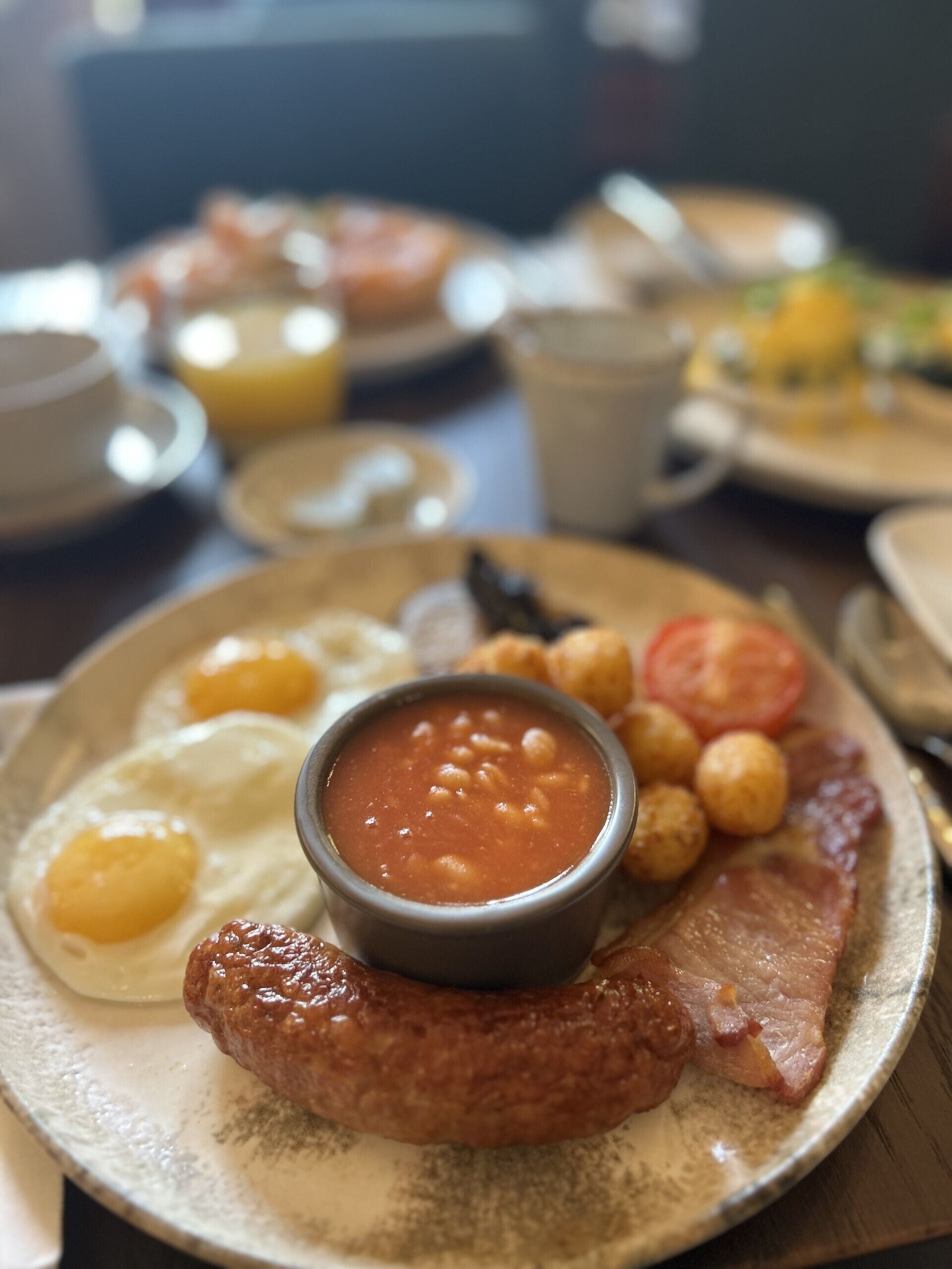 Une assiette de petit-déjeuner comprenant des œufs, des haricots, des saucisses, du bacon et un petit bol de sauce.