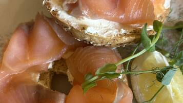 A sandwich with smoked salmon on a slice of bread, garnished with a sprig of herb and a lemon wedge.