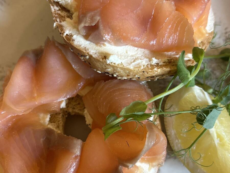 A sandwich with smoked salmon on a slice of bread, garnished with a sprig of herb and a lemon wedge.