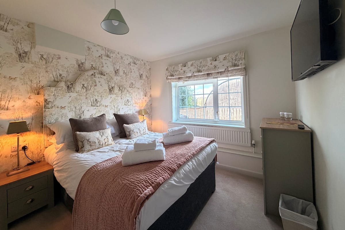 Une chambre à coucher comprenant un lit, une table de chevet, une lampe, une fenêtre et un téléviseur fixé au mur.