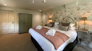 Een slaapkamer met een groot bed, twee bedlampen, een hoofdeinde met een bosdecoratie en een kledingkast.