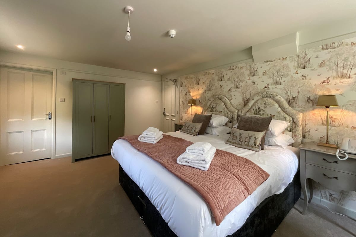 Une chambre avec un grand lit, deux lampes de chevet, une tête de lit ornée d’une fresque représentant une forêt et une armoire.