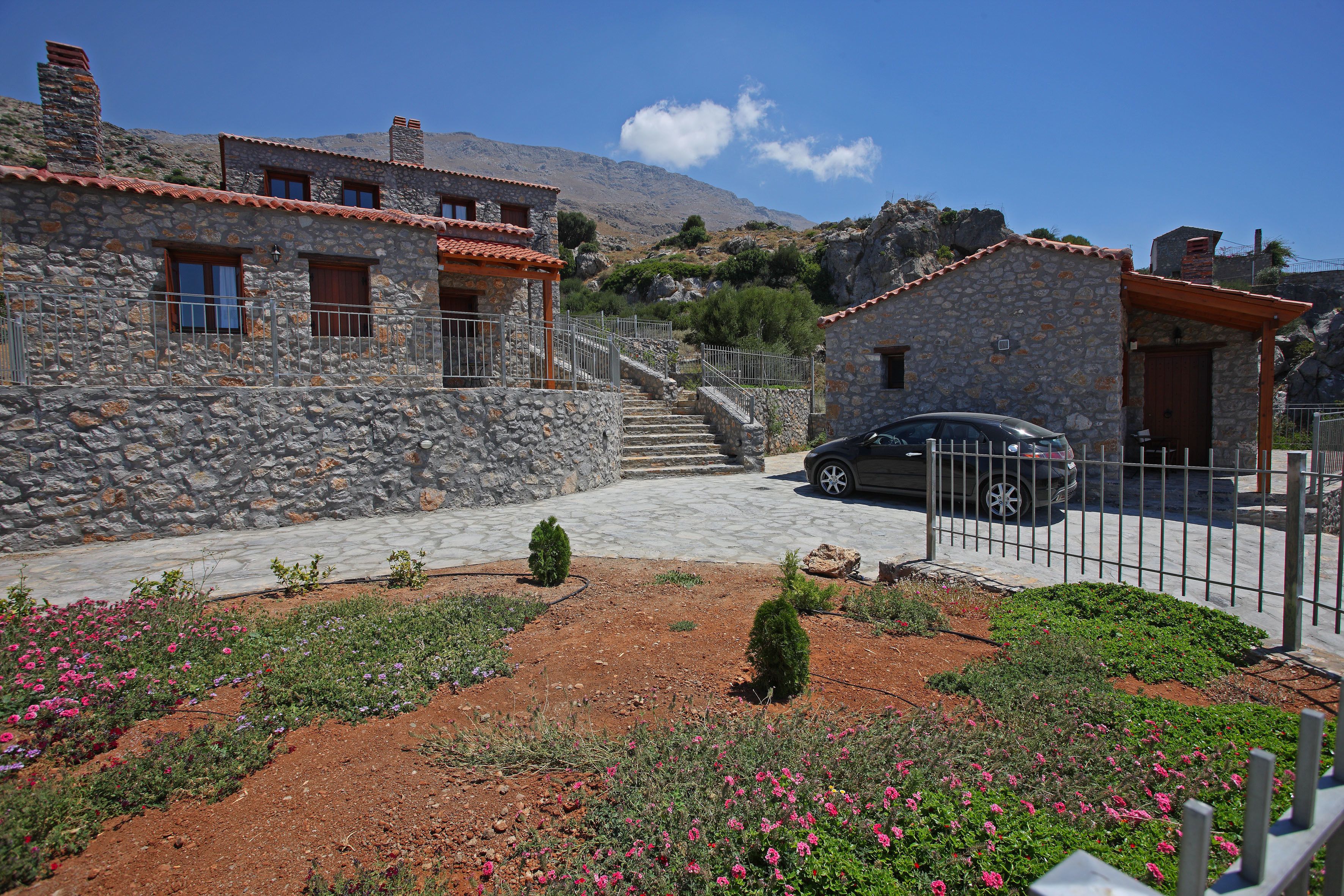 Un edificio in pietra con un'auto parcheggiata di fronte, circondato da un giardino fiorito di fiori rosa.