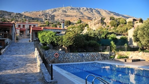A stone pathway leading to a swimming pool with a mountain backdrop. - Vrachos Villas (Agios Vasileios)
