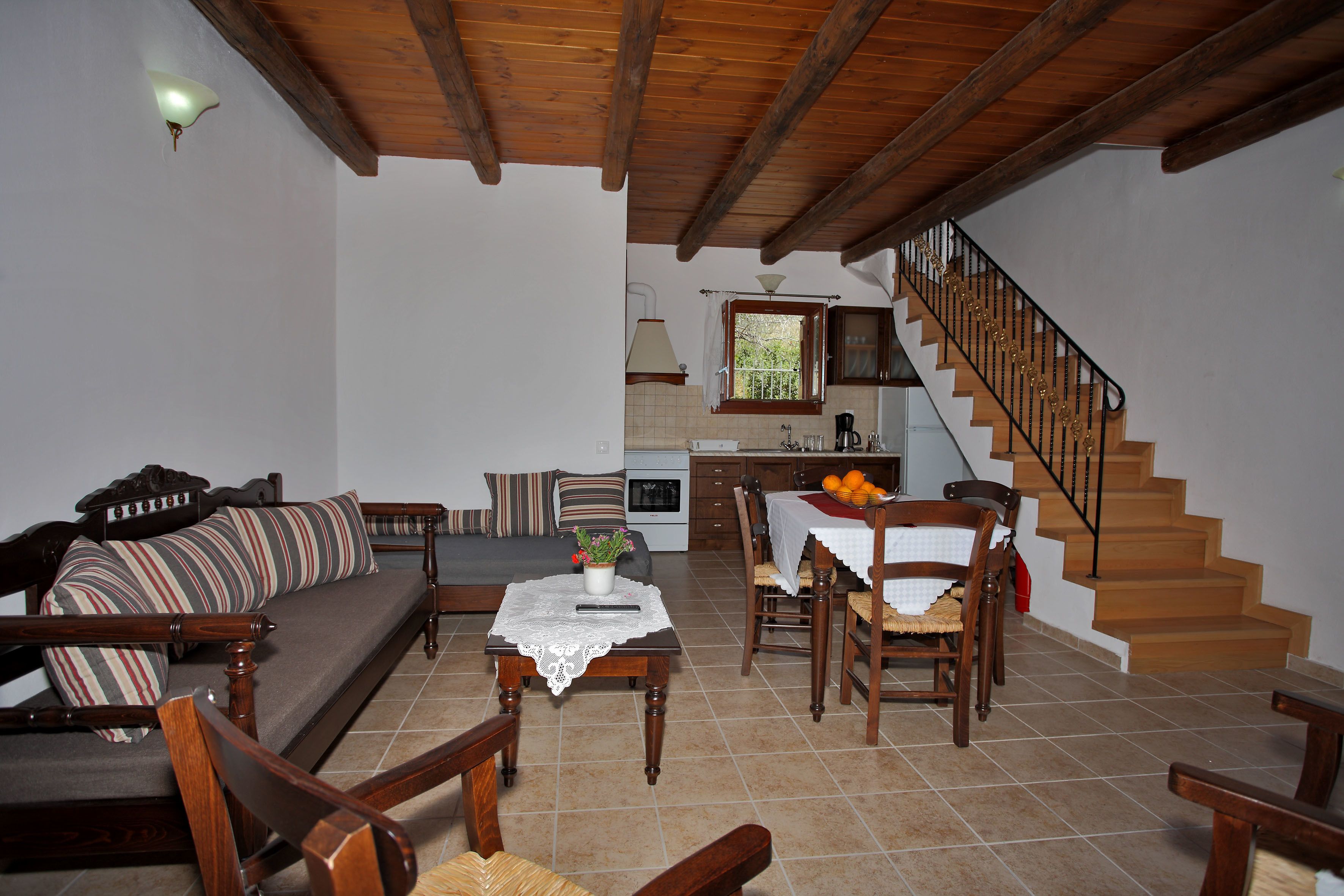 Ein Wohnzimmer mit Sofa, Sesseln, einem Esstisch und einer Treppe, die zur Küche führt.