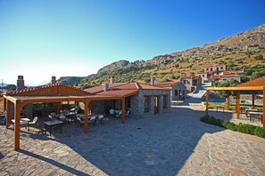 A stone courtyard with outdoor seating and stone buildings. - Vrachos Villas (Agios Vasileios)