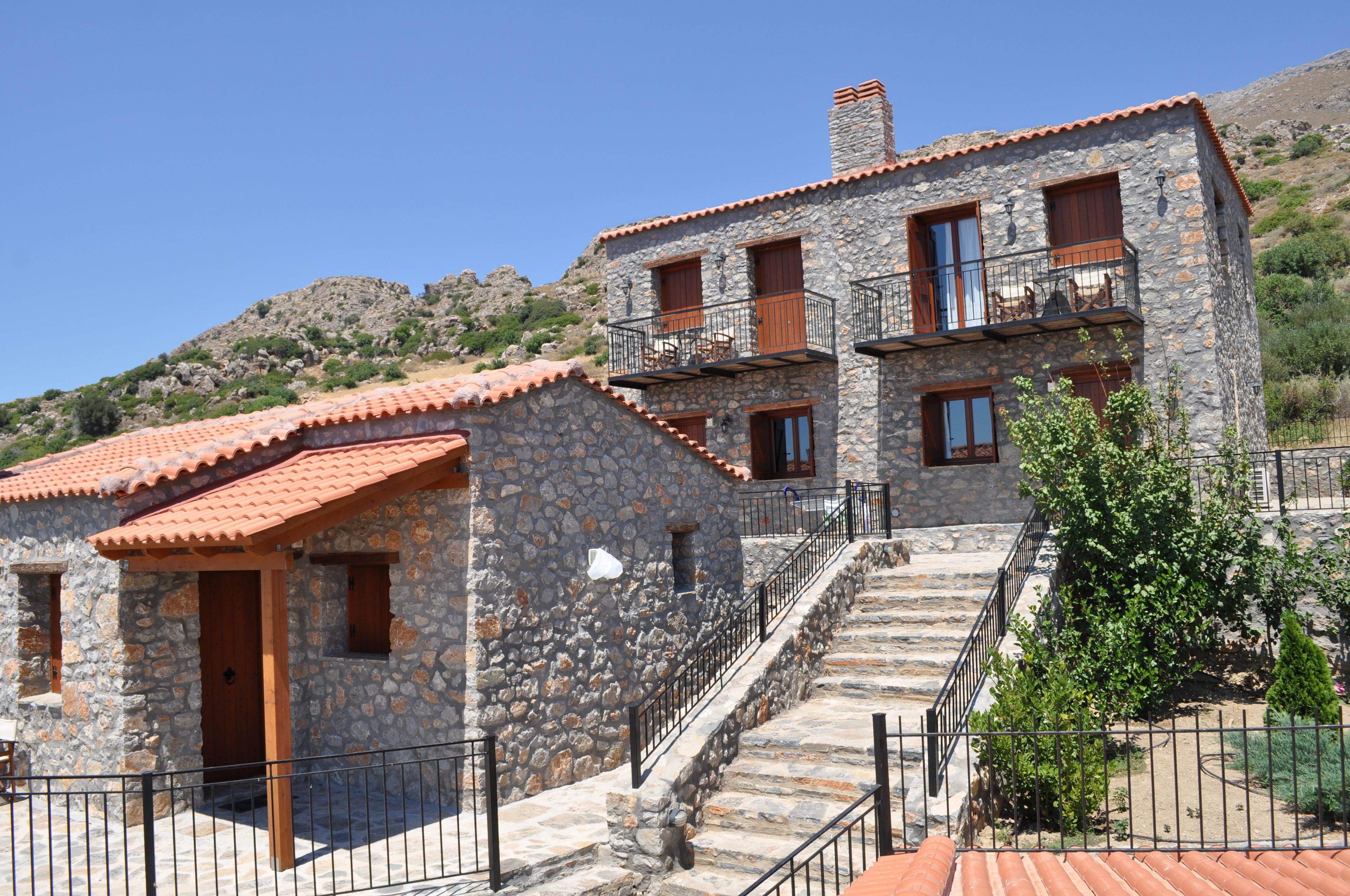 A stone building with a red-tiled roof, multiple windows, and a staircase leading to a balcony.