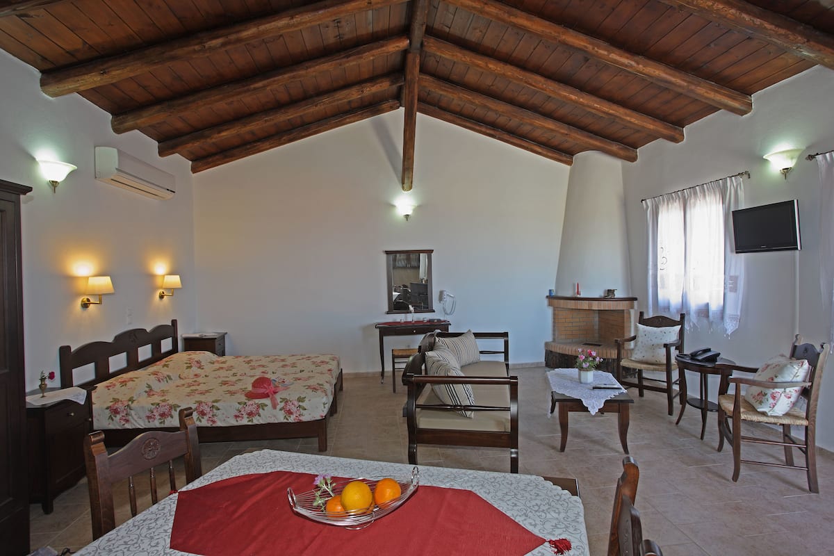 A cozy room with a wooden ceiling, a bed with floral bedding, a dining table with chairs, and a television on the wall.