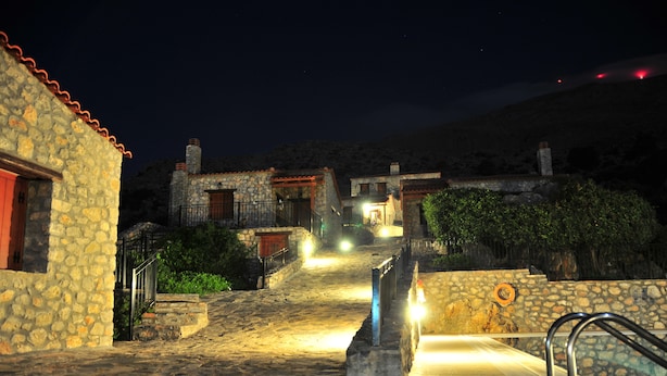 A stone pathway leading to a building with a red door, surrounded by greenery and stone walls. - Vrachos Villas (Agios Vasileios)