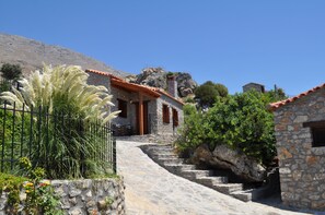 A stone building with a red-tiled roof, a staircase leading to a wooden door, and a view of a mountainous landscape. - Vrachos Villas (Agios Vasileios)