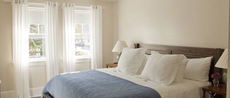 A bedroom with a bed, white curtains, a nightstand, and a lamp.