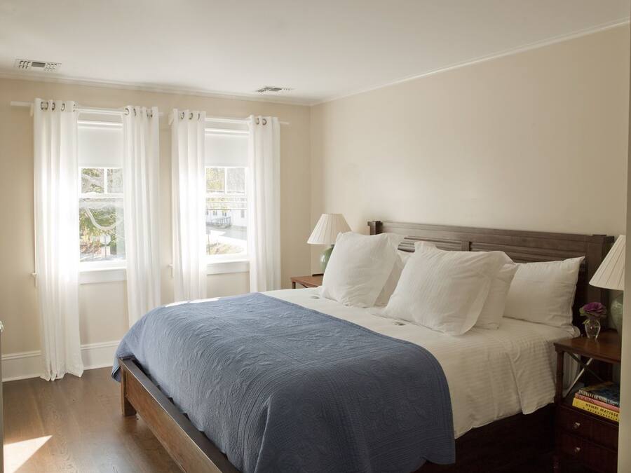 A bedroom with a bed, white curtains, a nightstand, and a lamp.