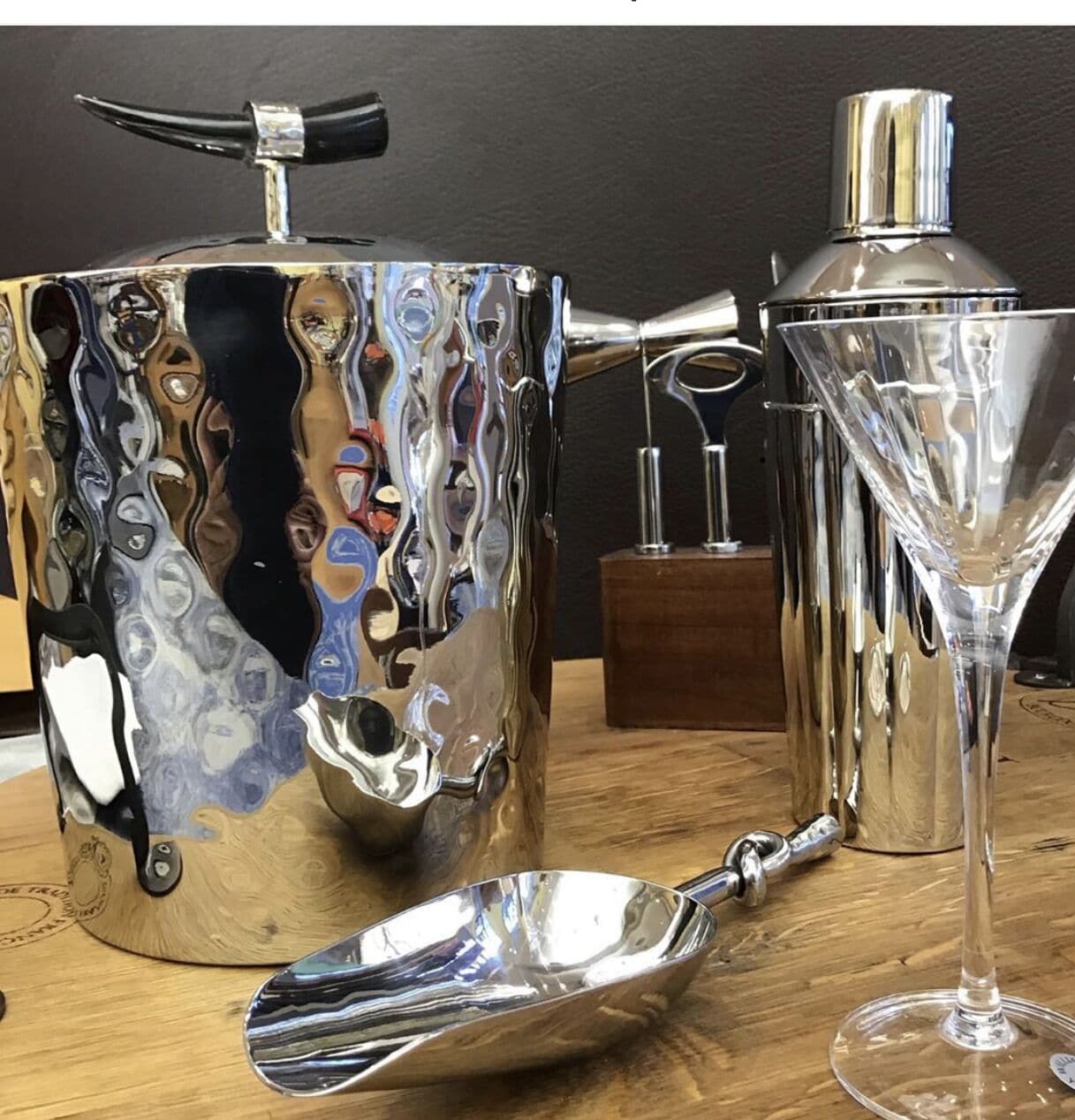 A metallic coffee pot, a cocktail shaker, and a martini glass on a wooden surface.