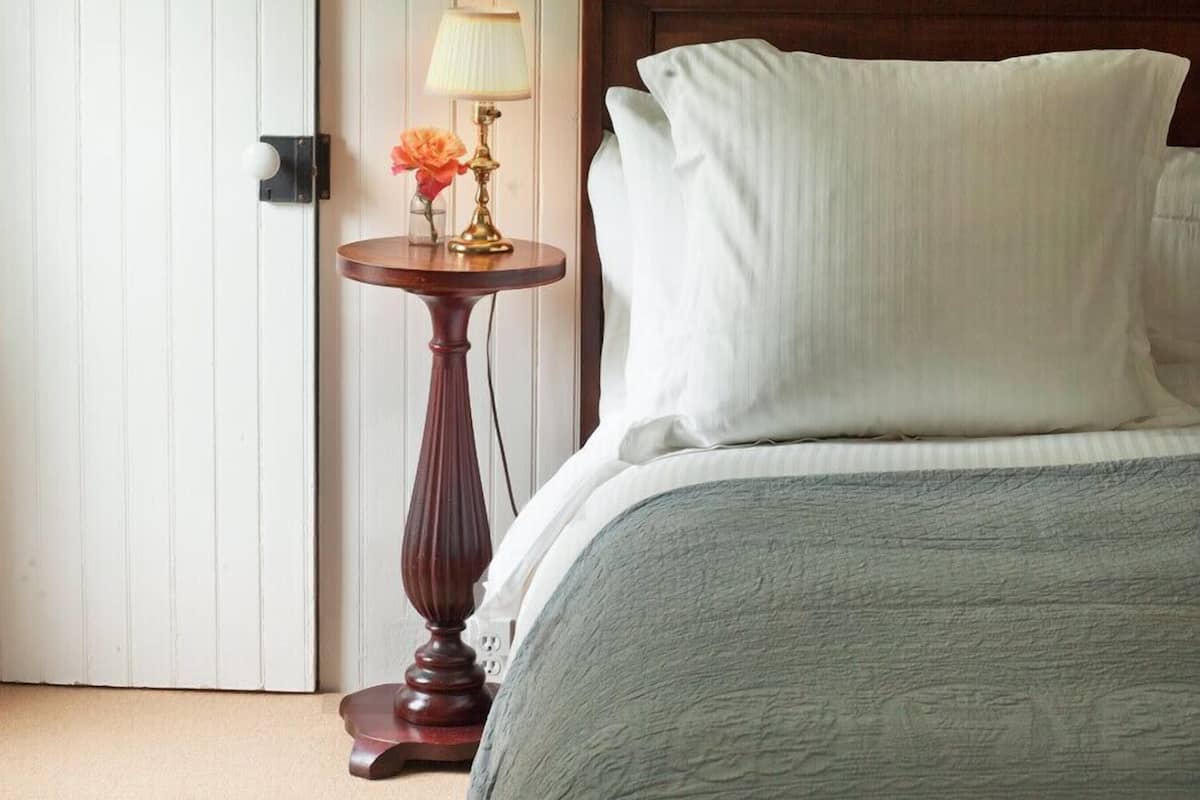 A bedroom with a wooden headboard, a bedside table with a lamp, and a bed with a grey blanket.