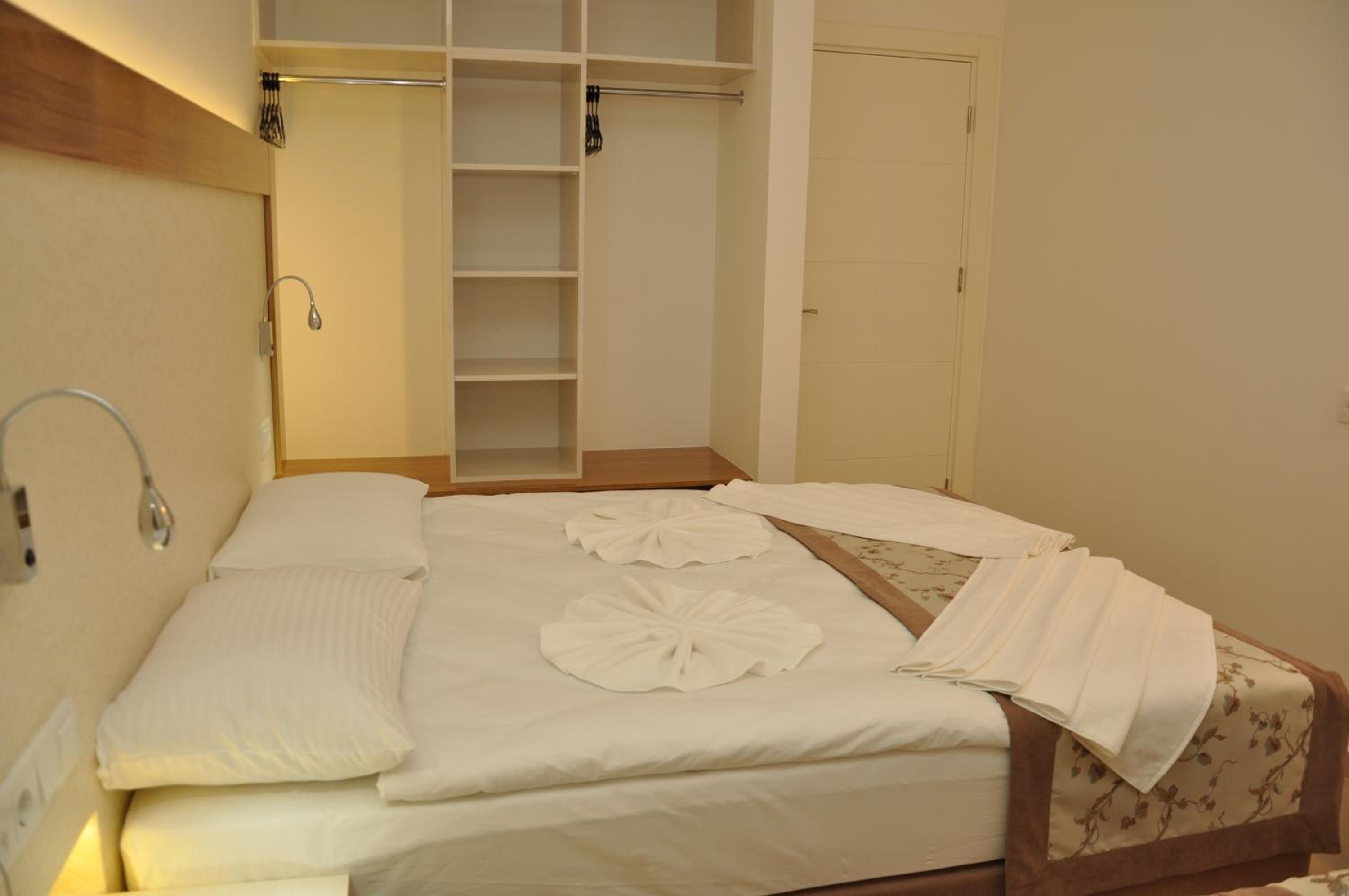 A hotel room with a neatly made bed, a wardrobe with hanging space, and a door.