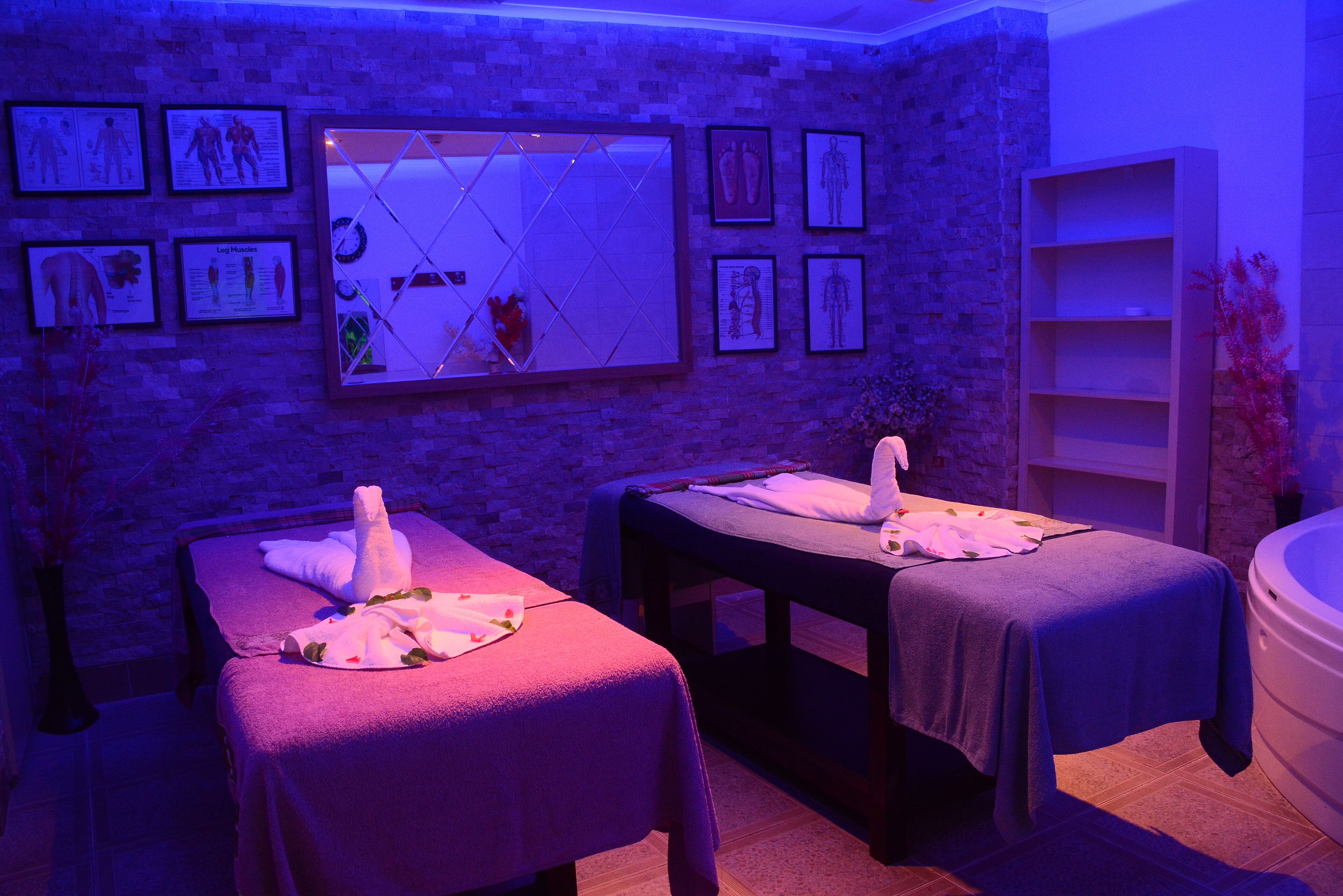 A spa room with two massage tables, a large mirror, and anatomical posters on the wall.