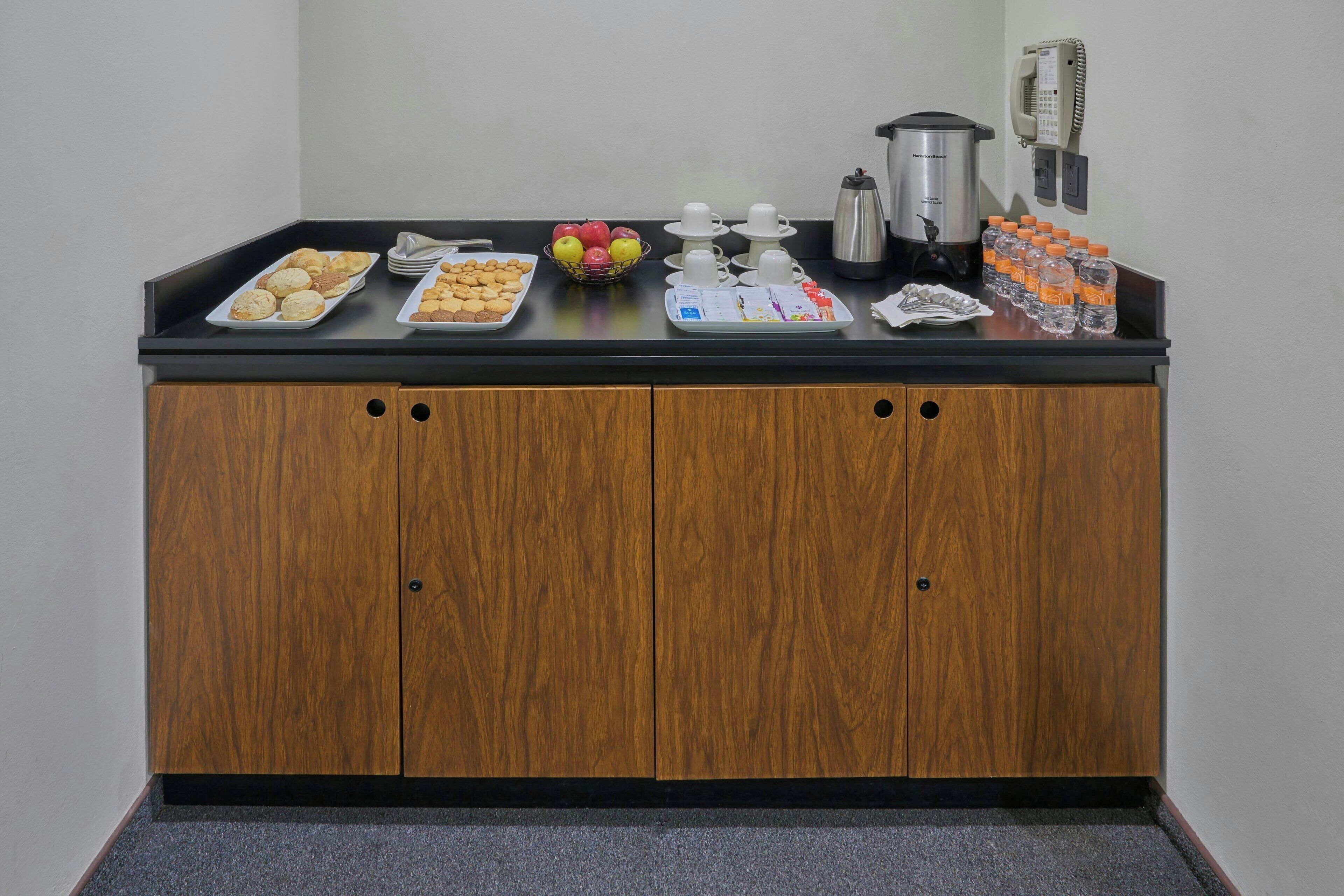 A breakfast bar with various food items, a coffee maker, and water bottles.
