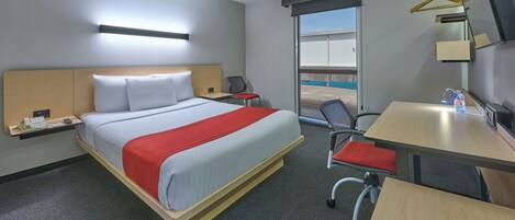 A hotel room with a bed, desk, chair, and a large window.