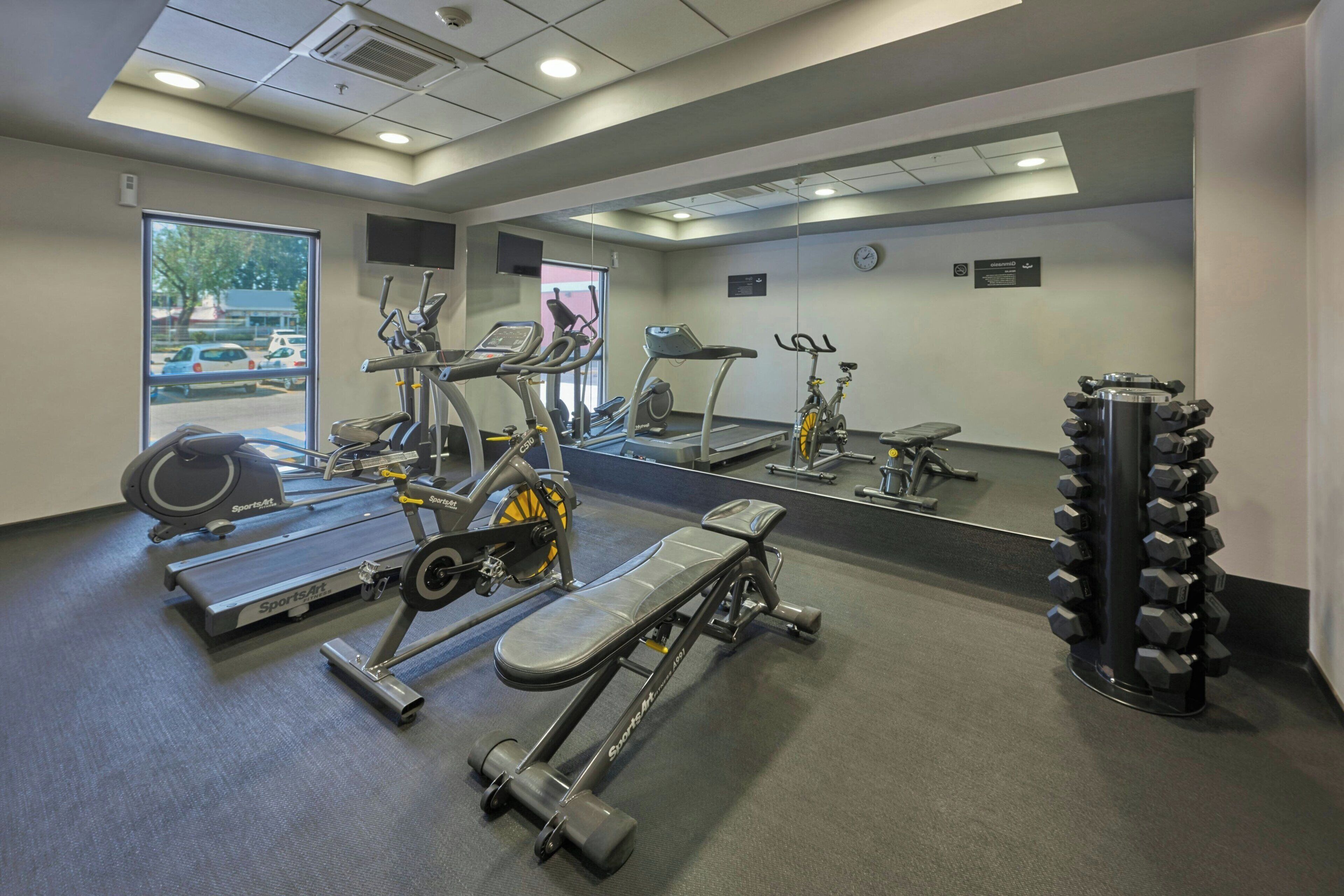 A gym with cardio machines, free weights, and a mirror.
