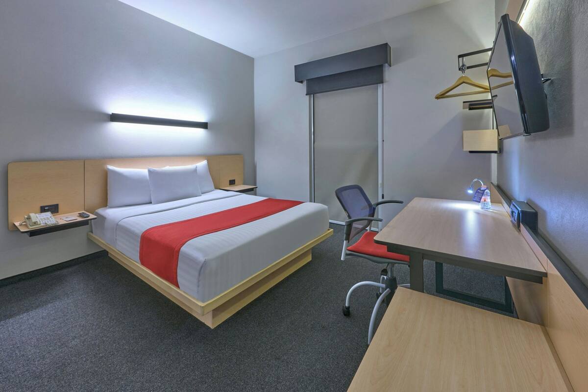 Ein Hotelzimmer mit Bett, Schreibtisch, Stuhl, Fernseher und Kleiderhaken.