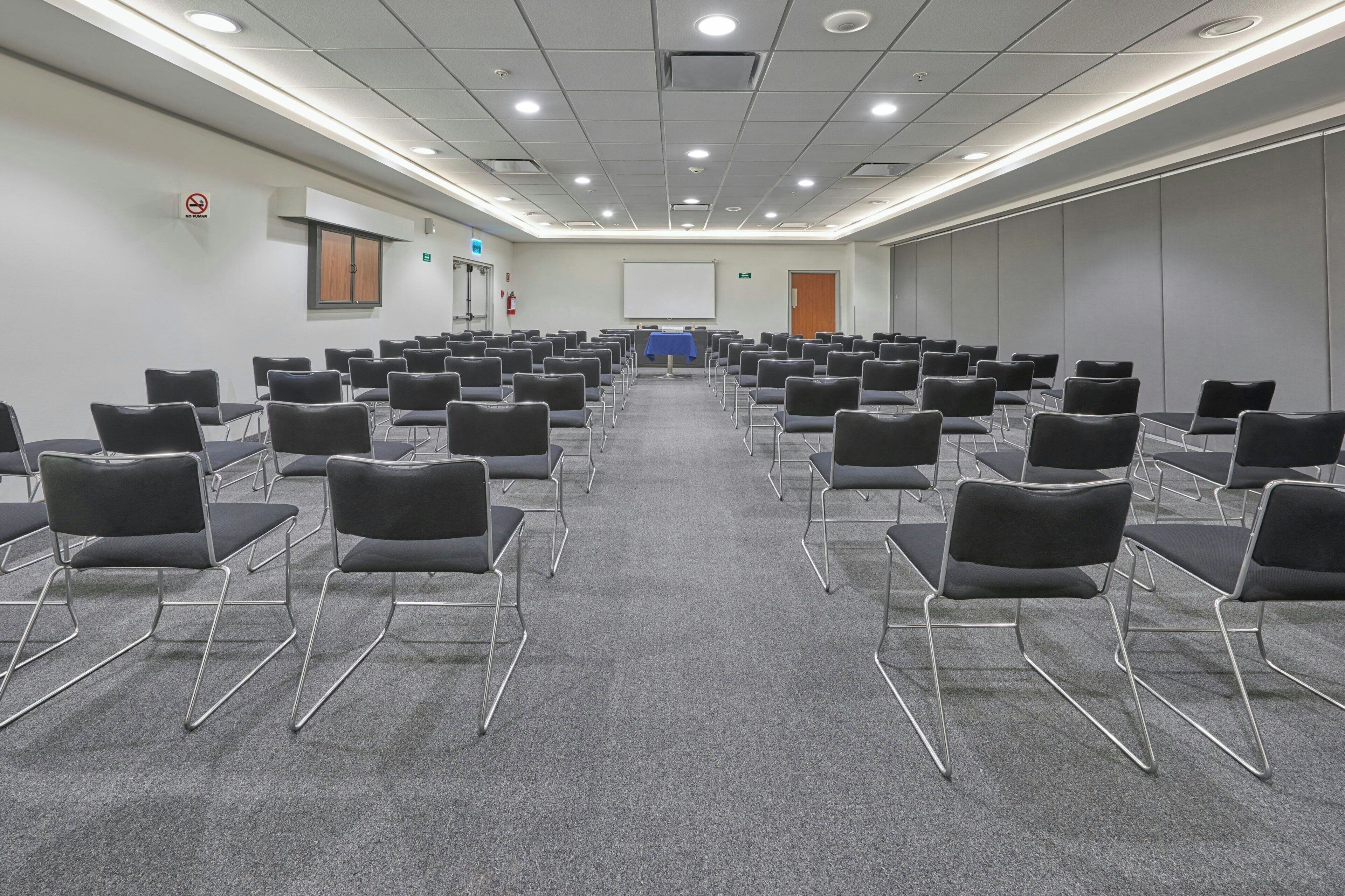 Ein Konferenzraum mit schwarzen Stühlen, einer Projektionsleinwand und einem Teppichboden.